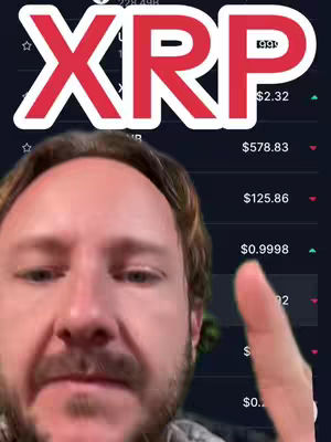 A man is shown in a selfie-style shot, with the word "XRP" in large, bold, red letters as a text overlay at the top. Below the text overlay is the face of a man with a beard and short brown hair. Behind him is a dark interface with what appears to be crypto currency data being displayed. The man is pointing with his right index finger towards the crypto data.