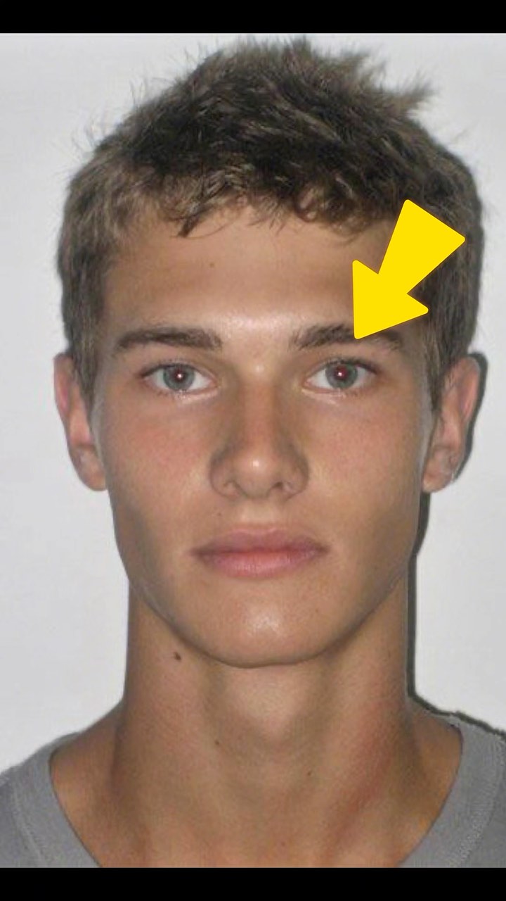 A close-up shot of a young man's face, with a yellow arrow indicating a part of the face. The man has short, dark hair, light skin, and blue eyes. He's wearing a gray shirt. The background is plain white.