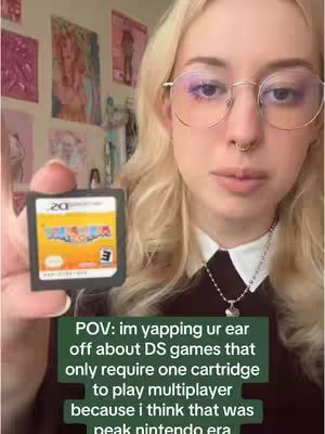 A young woman with blonde hair and glasses holds up a Nintendo DS game cartridge. She is in a room with posters on the wall behind her. Text overlays are present at the bottom of the image.