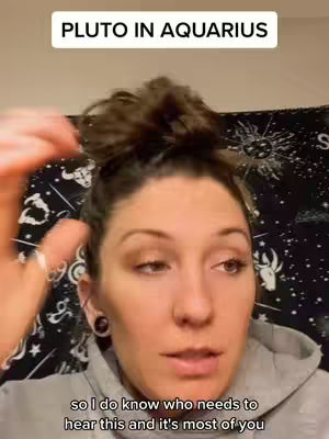 The cover image is a selfie-style shot of a woman from the chest up. She has light skin, brown hair styled in a bun, and dark eye shadow. She is wearing a gray hoodie and a small black earring. The background is a tapestry-like drape with a celestial design including moons and stars. Above her head is a white rectangular text overlay.
