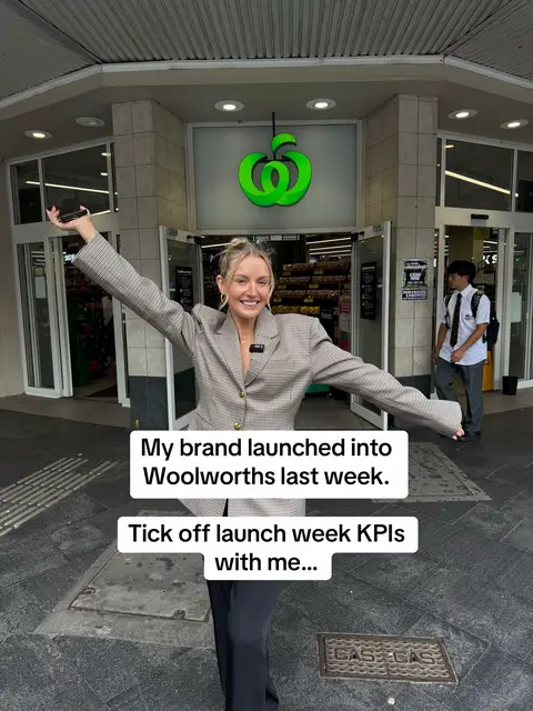 A woman in a grey blazer stands in front of a Woolworths store, arms outstretched in a celebratory pose. Text overlays are present.