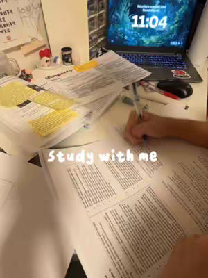 The image shows a desk with books, papers, a laptop showing 11:04 on the screen, a pen, small decorative items, and a hand writing on a book. The foreground features text that says 'Study with me'. The overall lighting is warm.