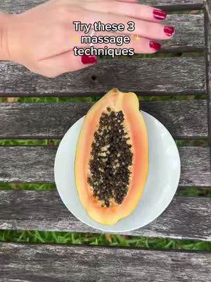 The image shows a top-down view of a cut papaya on a white plate, set on a wooden table with green grass peeking through the slats. A hand with red nail polish is positioned above, with text overlayed.