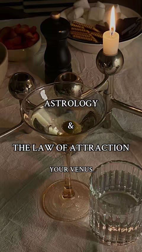 A flat lay photo showcasing a martini glass with a single olive; it is surrounded by objects that include a candle and other barware, set on a table.