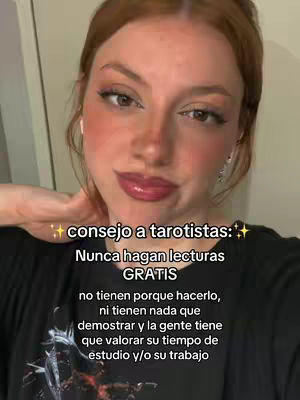 A selfie-style video cover image features a fair-skinned woman with auburn hair, smiling slightly. She wears a black top and has subtle makeup. The background is neutral. Overlayed text in white, with a yellow star and a soft glow around it, provides advice to tarot readers, emphasizing the importance of valuing their work and time. The image is well-lit, with a focus on the woman's face, promoting a personal message.