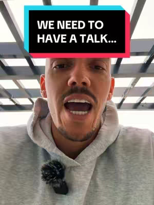 A man with a shaved head and a mustache is looking at the camera with his mouth open, as if speaking. He is wearing a gray hoodie and a small microphone is attached to it. Above him, a text box reads, 'WE NEED TO HAVE A TALK...'. The background is somewhat blurred, with what appears to be a ceiling made of light-colored beams in the blurry background.