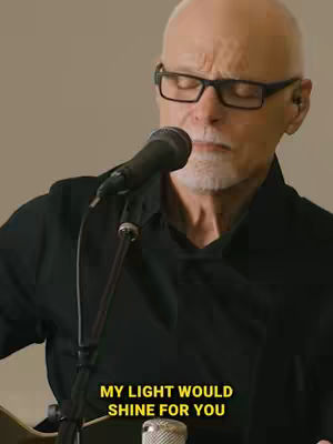 A close-up shot of an older man singing into a microphone, with text overlayed at the bottom.