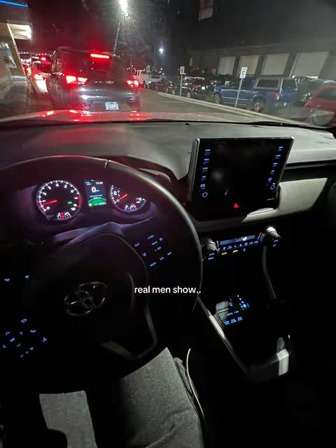 The cover image shows the interior of a car at night, from the driver's perspective. The dashboard and steering wheel are prominently displayed, with various gauges illuminated. Through the windshield, taillights of other vehicles are visible, suggesting traffic congestion on a city street. The overall lighting is dark and moody, with the glow of the car's interior lights creating a contrast with the external environment.
