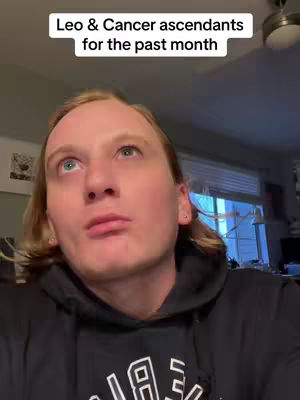 A person with long, light brown hair and a black hoodie looks upwards with a thoughtful expression. The background includes a ceiling fan and vague interior details.