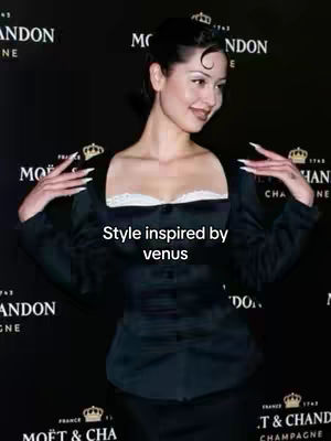 A woman with dark hair styled up, arms out, wearing a black top with a white neckline, against a backdrop with the Moët & Chandon logo.