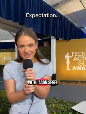 A woman with brown hair holds a microphone, facing the camera with a smile. She is standing in front of a backdrop adorned with the "Screen Actors Guild Awards" logo. Text overlays state 'Expectation...' and 'WITH JASON SEGEL'.