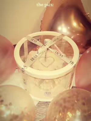 The cover image displays an overhead shot of a gift box. It's cylindrical with a clear plastic top and a creamy-white base. A ribbon is wrapped around the box with the brand's name is visible, and the top is decorated with heart, the background consists of soft pink and gold balloons.