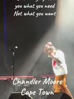 The image shows a stage performance at a concert. The artist is on stage in front of a dark background with stage lights creating bright streaks and spotlights. Text overlays include a motivational quote and the artist's name and location, with the artist gesturing with his hands. The scene is filled with an atmosphere of a live musical event.