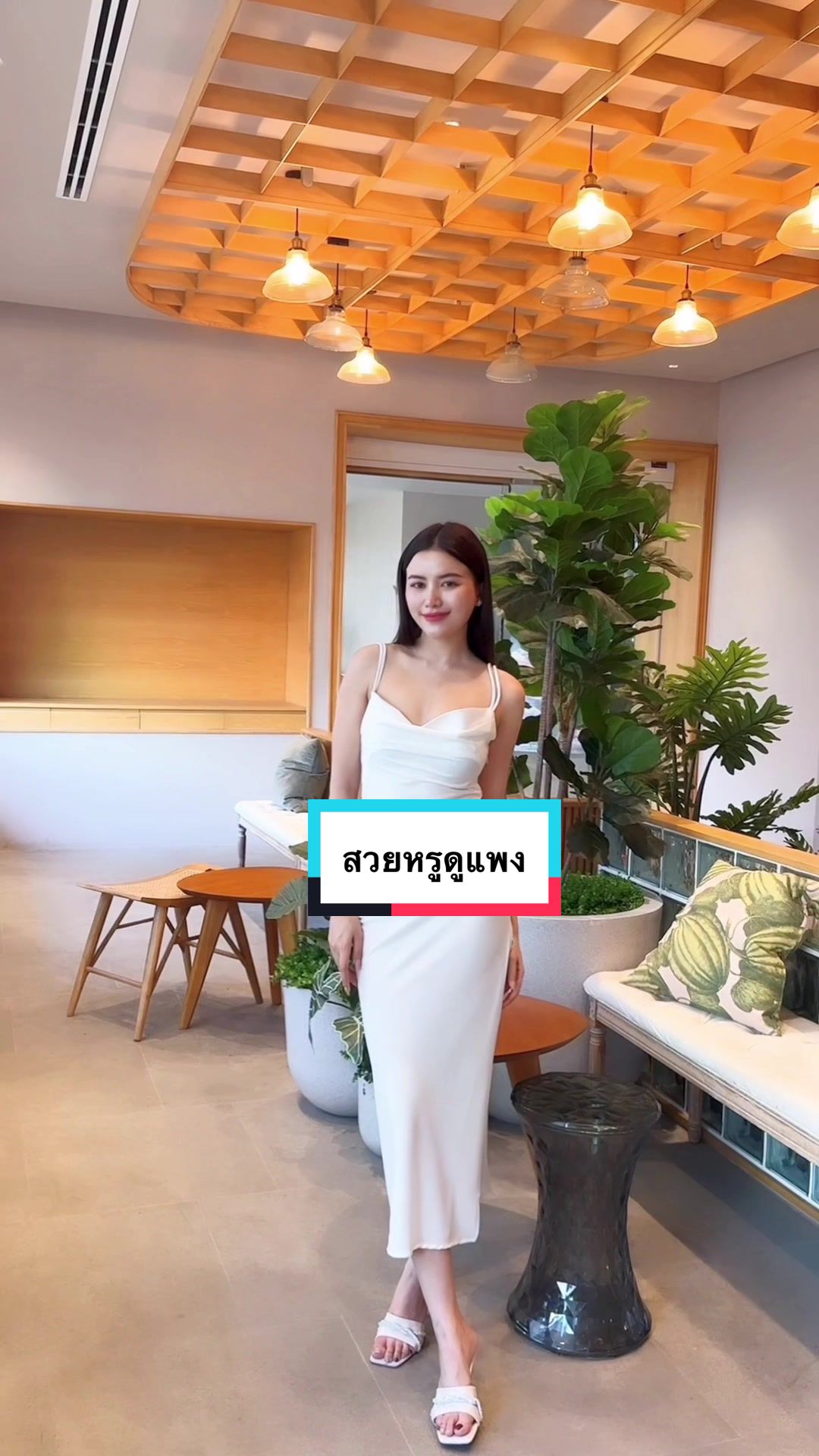 A woman in a white dress stands in a well-lit room with a modern interior. 