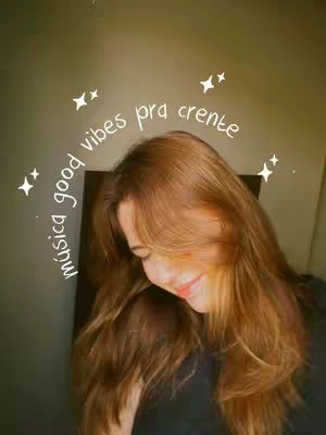 A woman with long, light brown hair is gazing downwards, her face partially obscured.  Text in a circular arc overlay announces "good vibes pra crente" with several white starbursts scattered around the text. The background is a blurred blend of olive green and beige, suggesting a soft, natural light.