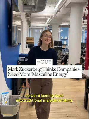 A well-lit interior shot featuring a woman standing and speaking. She is the primary focus, with a text overlay offering commentary on Mark Zuckerberg's views on 'masculine energy' in companies. Behind her, office or studio elements include desks, equipment, and a blue wall, creating a business-oriented setting. Neutral colors and the woman's attire suggest a casual yet professional environment.