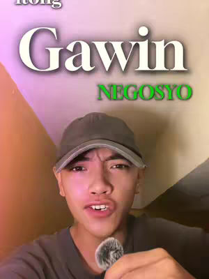 A young man with a gray baseball cap and a dark shirt is holding a microphone, looking directly at the viewer. Above his head, large text overlays read "Gawin", and below it, the word "Negosyo" is displayed, suggesting a message or tutorial.