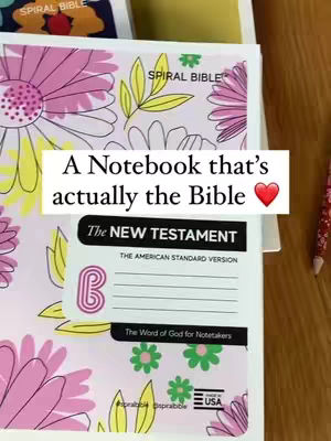 The image shows a Bible open to the pages of the New Testament. A white rectangular label is overlaid across the pages, with the text "A Notebook that's actually the Bible" displayed in a handwritten style. The background has pink and yellow floral patterns.