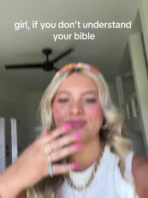 A selfie-style video cover image featuring a young woman. She is fair-skinned with blonde hair, styled with loose waves, and a colorful headband. She's wearing a white top and pink lipstick. Her hand is raised towards her face, with bright pink nail polish on her fingers. The background appears to be a home setting, with a ceiling fan visible. Text overlayed on the image reads, "girl, if you don't understand your bible".