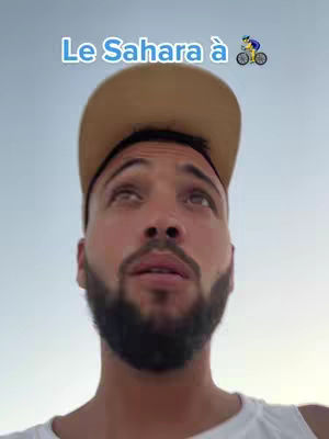 A man with a beard and a cap looks upwards with the sky in the background. Text in French is overlaid at the top.