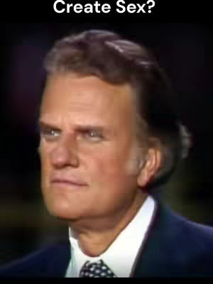 A medium shot features a man, likely the subject of the video, centered in the frame. He is a fair-skinned individual with short, combed-back hair. He’s wearing a dark suit jacket over a white shirt, and a patterned tie. The image has a soft focus, giving it a classic, somewhat aged aesthetic.