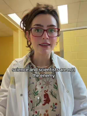 A woman with brown hair and red glasses in a brightly lit room. She is wearing a white lab coat over a patterned shirt. Text overlayed on the image reads, "science and scientists are not the enemy".