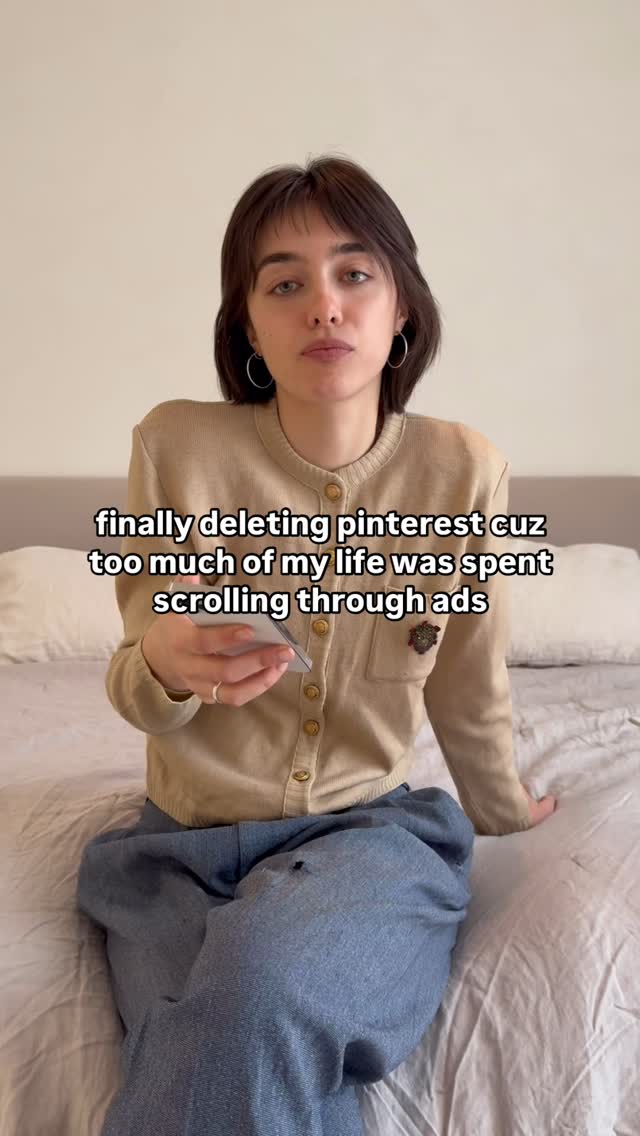 A woman is sitting on a bed, looking at the camera while holding a phone. The lighting is soft, and the color palette is natural, with a beige cardigan and light blue jeans. Text is overlaid on the image.