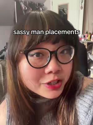 A woman with glasses is looking directly at the camera and speaking, overlaid with text. She has dark hair and medium skin. The background is a blurred interior with items visible on shelves or a table.