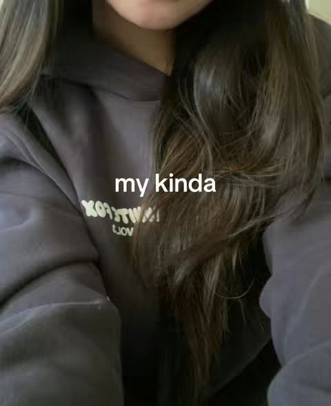 The image presents a close-up shot of a person, likely a young woman, with long, dark hair. The top of a dark gray hoodie is visible, with text partially obscuring the design. The overall composition is simple, focusing on the hair and clothing, with the text overlay adding a declarative element.