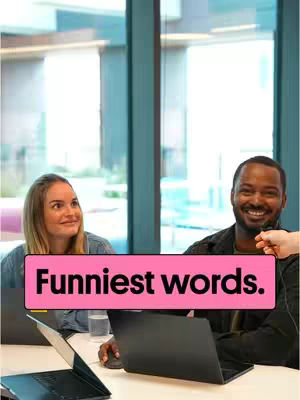 The cover image shows two people, a woman with blond hair and a man, both looking off to their left, seated at a table in what appears to be an office setting. A pink rectangle overlay with the text 'Funniest words' is positioned in the center of the image. Beside them is a laptop and a glass of water, suggesting a casual yet professional atmosphere. The background features a large window with daylight.