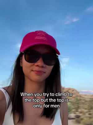 A selfie-style shot featuring a woman wearing a pink cap and sunglasses, set against a backdrop of a bright blue sky and blurred natural scenery. Text overlay at the bottom reads, "When you try to climb to the top but the top is only for men."