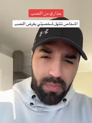 A man with a beard wearing a black cap and a white hoodie is in the foreground against a blurred background. Red and white text banners are overlaid on the image. The man appears to be looking toward the camera with a neutral expression, with a hint of concern.