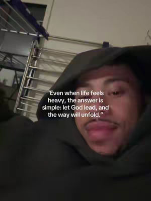 A selfie-style shot featuring a person in a hooded sweatshirt. The person is centered, with their face visible and a quote overlaid on the image. The background is blurred, with glimpses of a metallic ladder or shelving unit. The image has a slightly warm tone.