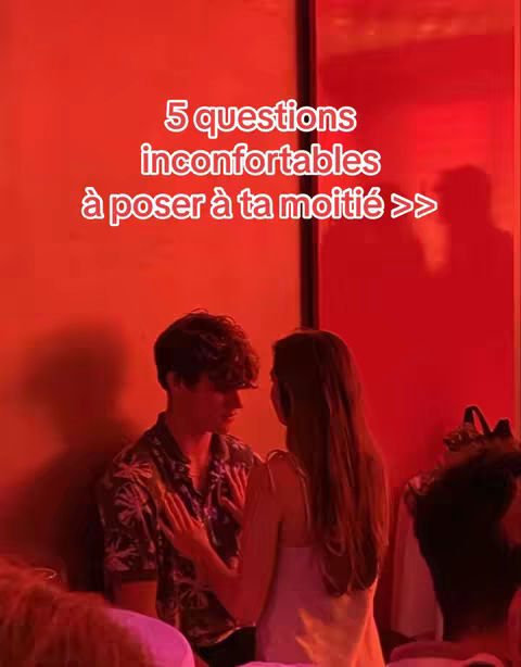 A couple is seen in a dimly lit room with red lighting. The man is on the left with curly hair looking down. The woman is on the right. Text overlays the image in the center.