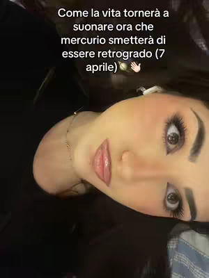 A close-up shot of a woman's face, angled slightly upward. She has prominent eye makeup and full, glossy lips. The background is dark, which accentuates her light skin and features. Text in white is placed above her head.