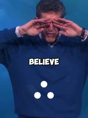 A man with graying hair wearing a blue sweater holds his hands up to his eyes, as if shielding them. The word 'BELIEVE' is in a bold, white font across his chest. Below, three white circles are arranged in a triangle shape.
