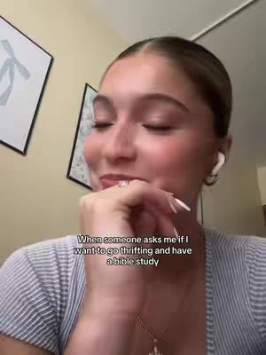 A close-up shot of a woman with fair skin, light brown hair pulled back, and a light blue striped shirt. She has earrings and white earbuds in. Her hand is raised to her chin. Text overlayed says 'When someone asks me if I want to go thrifting and have a bible study'.