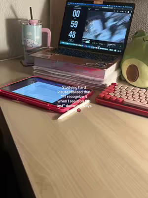 The image shows a workspace setting, with a light-colored wooden surface serving as the base. On this surface, there's a laptop displaying a timer, a tablet, a keyboard, a cup, and a stuffed animal. The laptop's screen dominates the view, showing what appears to be a timer counting down. The tablet is positioned in front of the laptop and a pen is nearby, suggesting a focus on digital note-taking or design. The keyboard is positioned to the right and has a red color scheme. The cup, with a specific and cute design, adds a touch of personalization to the scene. A cute avocado-shaped stuffed animal is placed in the background. The overall composition suggests a study or work session with focus on time management and digital tools. The text overlay in the image provides context and may be a hook to the content.