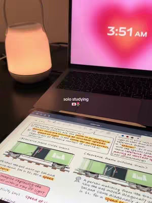 A nighttime study scene. A laptop displays a heart-shaped clock at 3:51 AM. Beside it, a bright, rounded lamp glows. Below, notes on a tablet show diagrams and handwritten annotations, suggesting physics concepts. The overall mood is focused and academic.