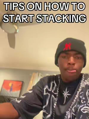 A young man wearing a black beanie with a red "M" on it and a black shirt with a white cross and some star designs is looking at the camera. The background is a room with a ceiling fan and some sort of artwork on the wall. The hook text reads "TIPS ON HOW TO START STACKING".