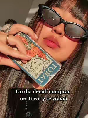 A close-up shot of a woman holding a tarot card, wearing sunglasses and holding the card near her face, with overlaid text at the bottom.