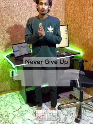 A man in a green Adidas sweatshirt stands in front of a desk with computer screens. The image has a text overlay that says 'Never Give Up'.
