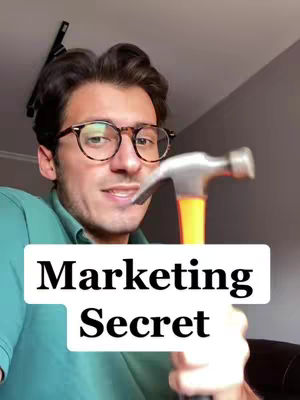 A man wearing glasses and a green shirt holds a hammer in front of him, with a text overlay that reads 'Marketing Secret'. The background is a muted gray.