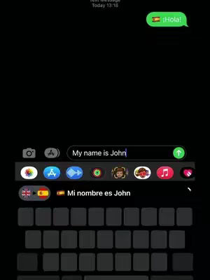A screenshot of a phone screen displaying a messaging app interface. The screen shows a text conversation.  At the top right, a speech bubble with the word "¡Hola!" and a Spanish flag emoji is visible. Below, in the text entry field, the words "My name is John" are displayed with a blinking cursor.  Above the keyboard, a suggestion "Mi nombre es John" is displayed. The rest of the interface includes the app's icons and keyboard.