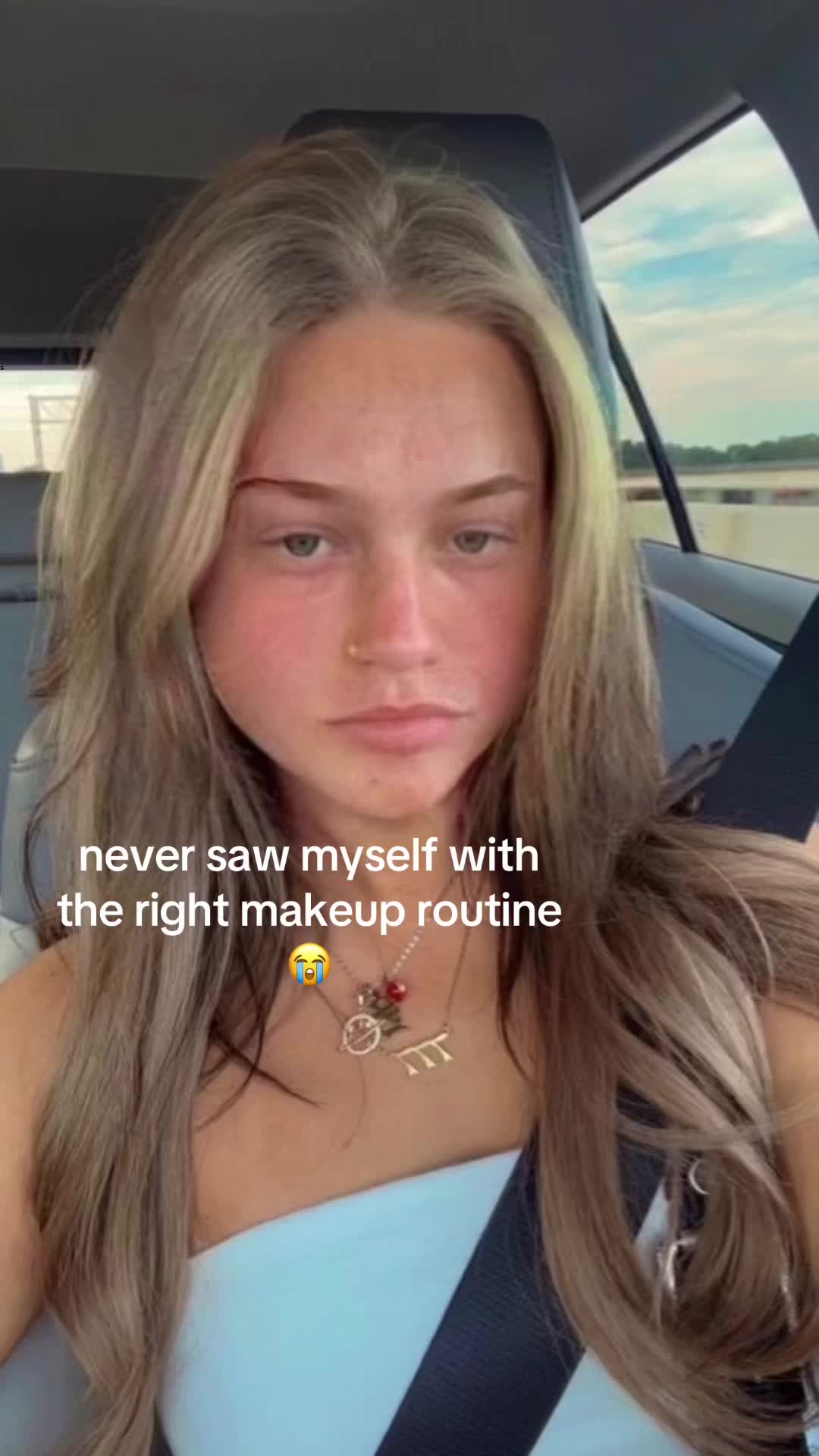 The cover image is a selfie of a young woman in the driver's seat of a car. Her long, light-colored hair is parted on the side and falls over her shoulders. She has a neutral expression, slight red blush on her cheeks, and is looking towards the camera, and has a nose piercing and simple necklace. The background is blurred, suggesting motion, and a portion of the car's interior can be seen.