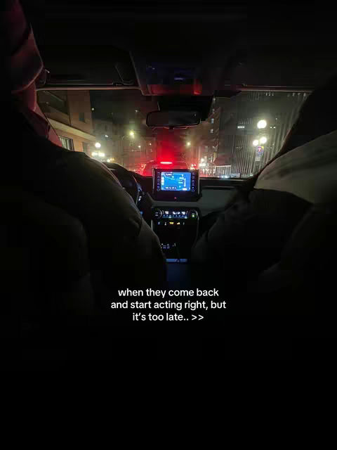 A nighttime driving scene viewed from inside a car. The interior is dark, but streetlights illuminate a city scene outside the windows. The focus is on the dashboard, with a screen displaying a map and controls.