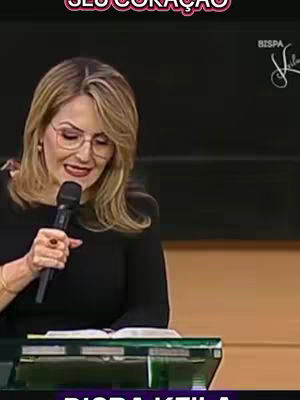 A woman wearing glasses speaks into a microphone, holding it with her left hand. She is positioned behind a podium with a book. The background is a blurred dark color. Text overlay is written at the top and bottom of the cover image.