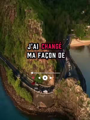 The cover image is a scenic aerial shot of a coastal landscape featuring a winding road, lush green hills, and a body of water. The central element is a text overlay that reads 'J'AI CHANGÉ MA FAÇON DE'. The scene is framed in a vertical orientation, with the road snaking through the landscape alongside the water's edge.