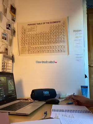 The cover image shows a well-lit desk setup with a laptop displaying a screen, a JBL speaker, and a notebook. A periodic table chart hangs on the wall, and the image is framed from a slight angle, suggesting a study or work environment.