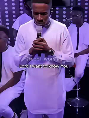 A man in a white outfit is centered, holding a microphone and looking down with his hands clasped. The background is blurred but suggests a stage setting with other individuals. Text overlayed on the image reads: 'Lord I want to know You'.